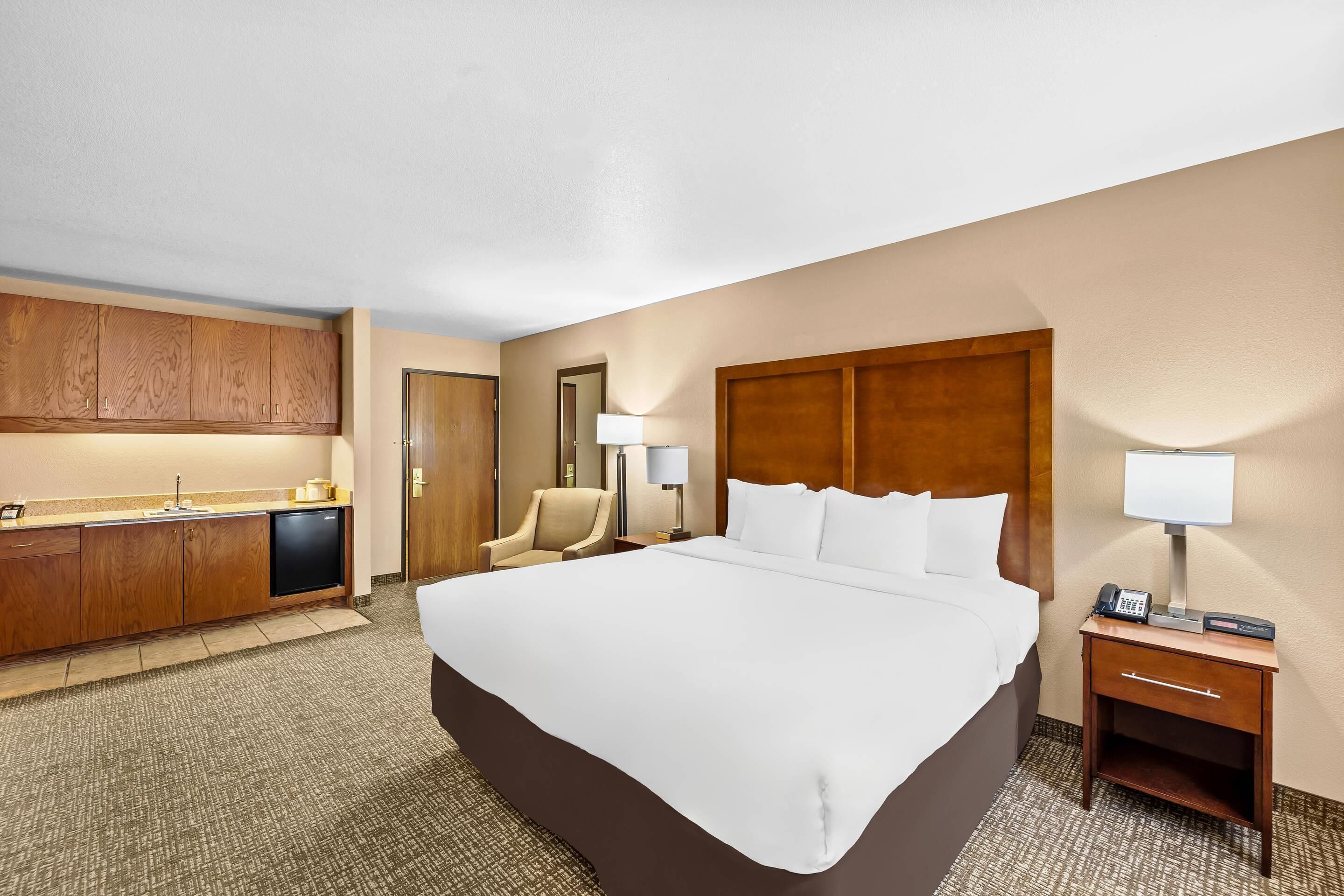 Habitación de hotel con una cama grande, un escritorio con lámpara, una silla, un minibar y la puerta del baño.