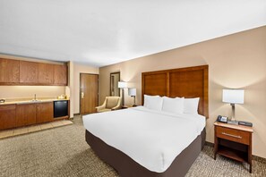 A hotel room with a large bed, a desk with a lamp, a chair, a minibar, and a bathroom door. - Comfort Inn Benson near Kartchner Caverns (Benson)