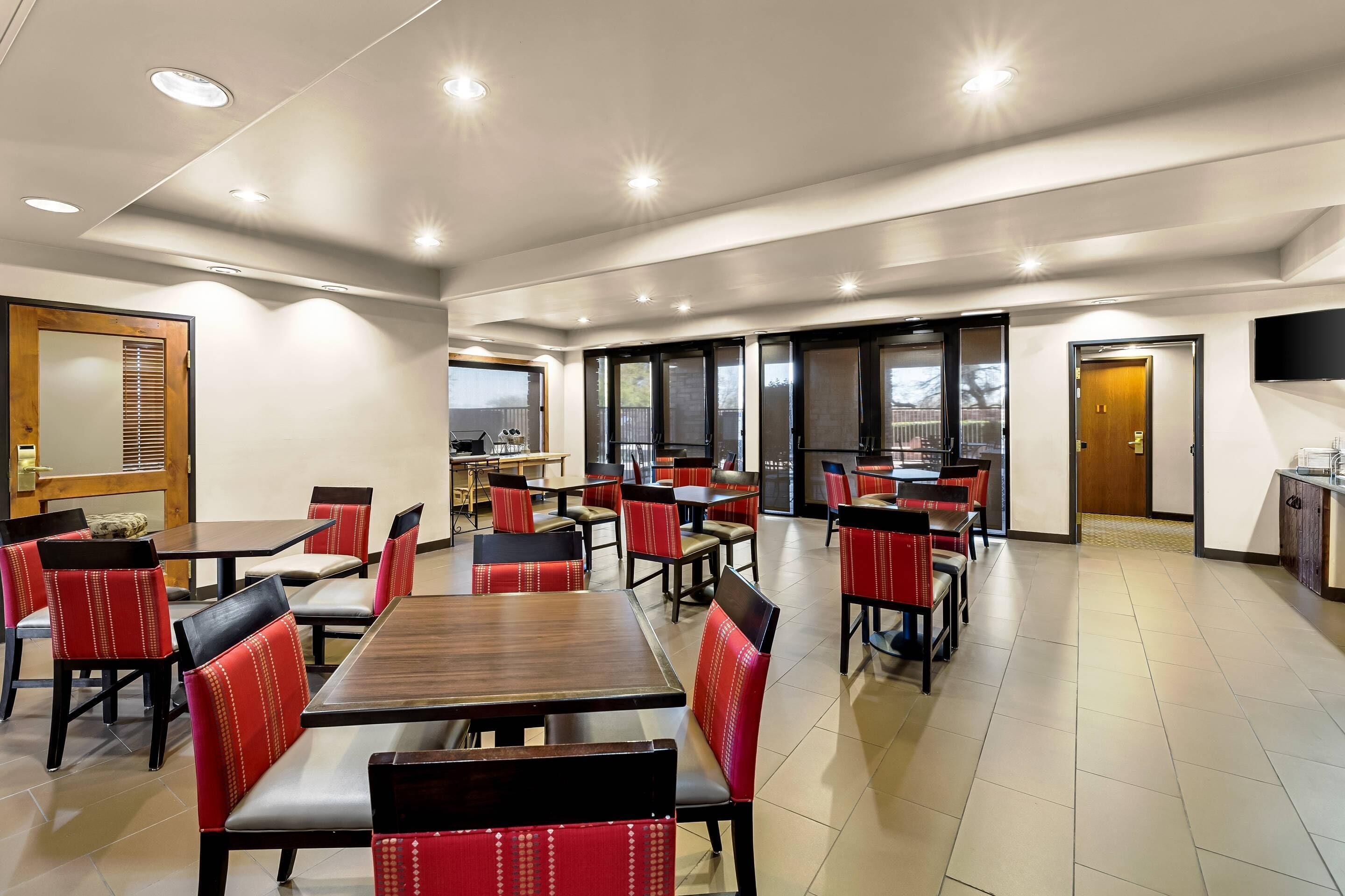 Un comedor amplio e interior con varias mesas y sillas, un televisor de pantalla plana montado en la pared y vistas a través de puertas de vidrio.