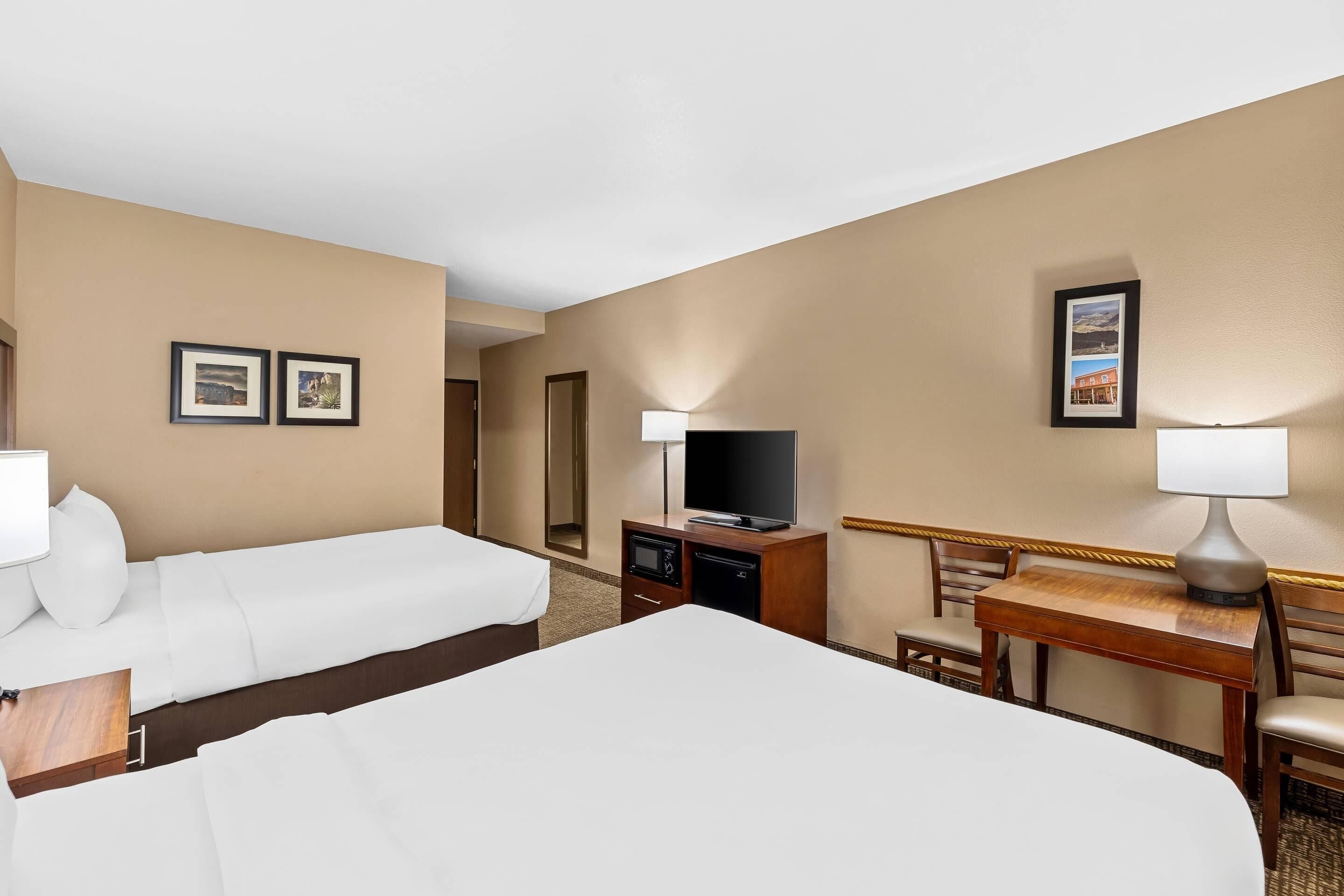 A hotel room with two beds, a desk with a chair, a television, and framed pictures on the wall.