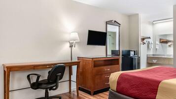 Ein Hotelzimmer mit Holzschreibtisch, schwarzem Bürostuhl, Bett mit roter und beiger Bettdecke, flachbildfernseher an der Wand, Mikrowelle und kleinem Kühlschrank.