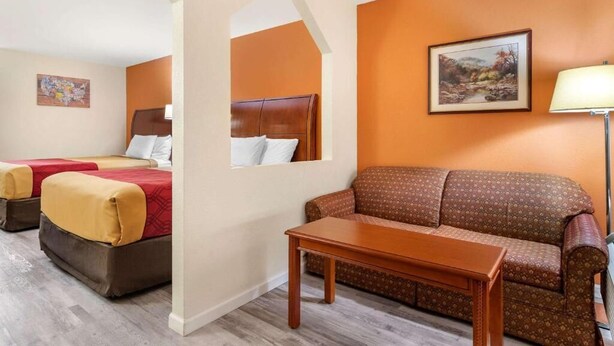 A hotel room with two beds, a sofa, a table, and a painting on the wall. - Kings Inn (LaFayette)