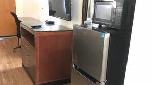 A compact kitchenette with a refrigerator, microwave, and a flat-screen TV on a wooden desk. - Kings Inn (LaFayette)