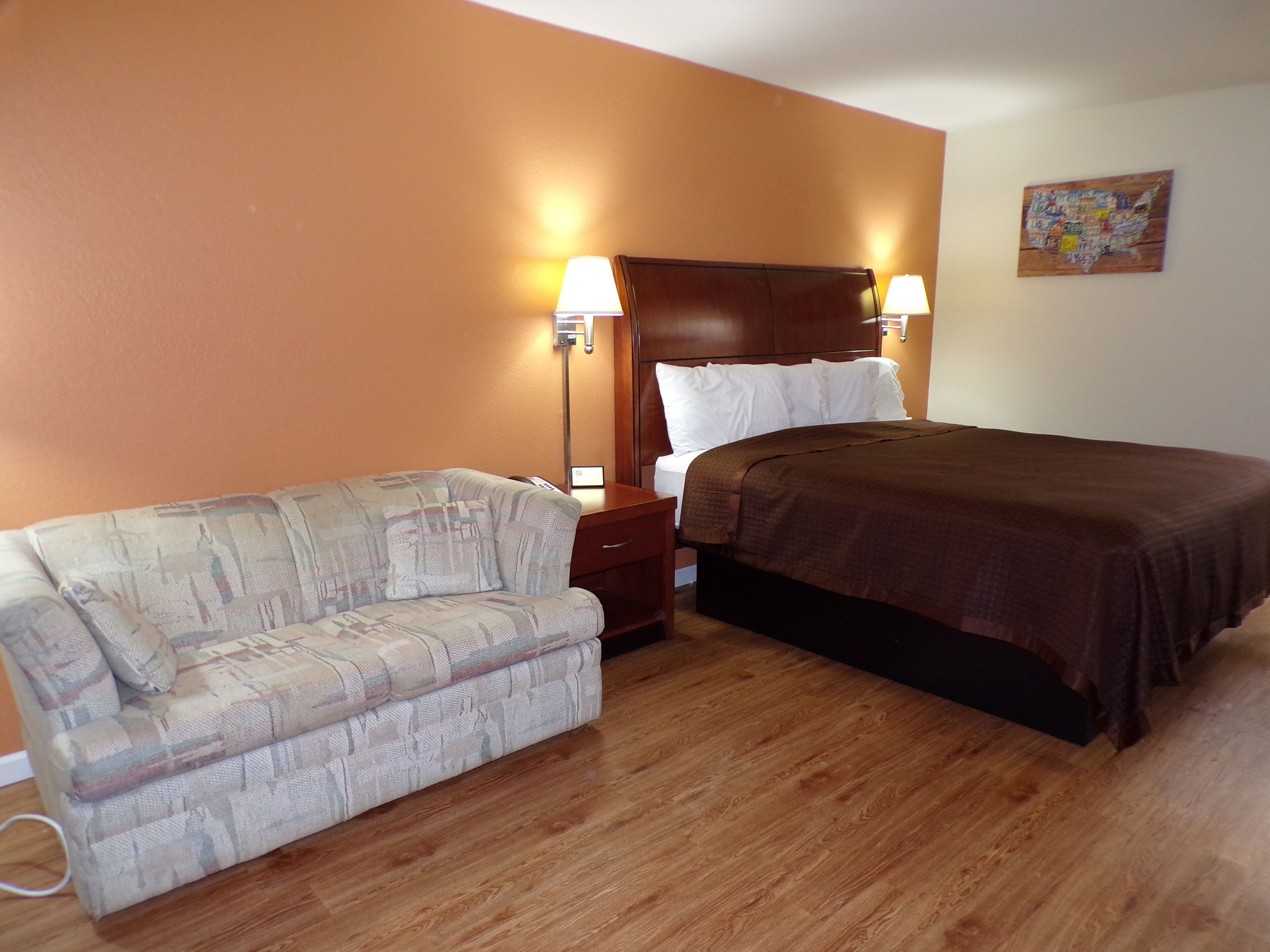 A hotel room with a bed, a sofa, a nightstand, and a wall-mounted lamp.