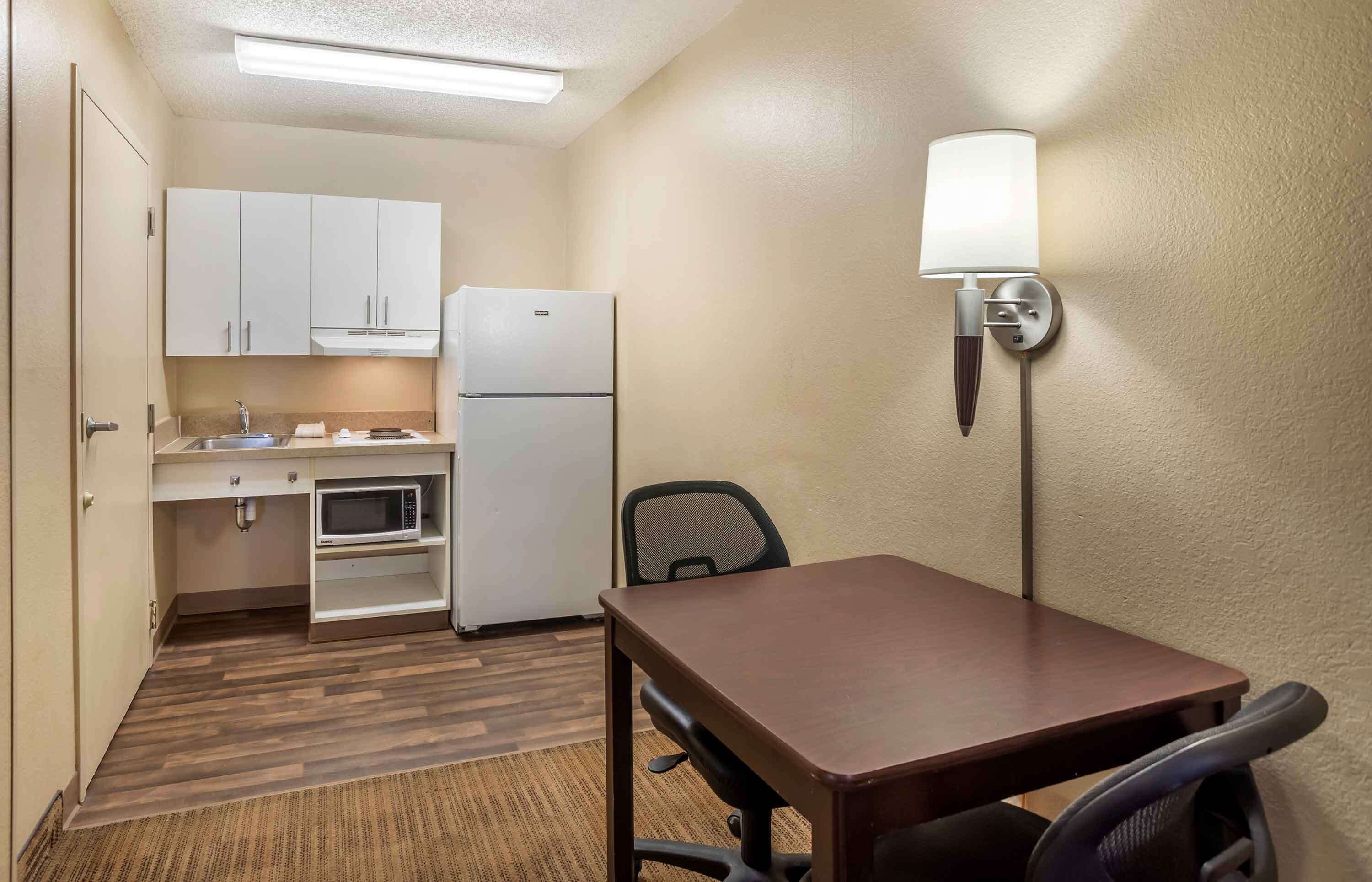 A compact hotel room with a kitchenette, a dining table, and a single chair.