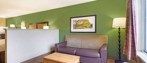 Una habitación con pared verde, sofá morado, mesa de madera, mostrador de recepción y un cuadro enmarcado.
