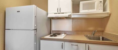 A compact kitchen with a refrigerator, microwave, stove, sink, and cabinets.