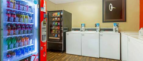 A laundry facility with a Coca-Cola refrigerator, a vending machine, and three washing machines.