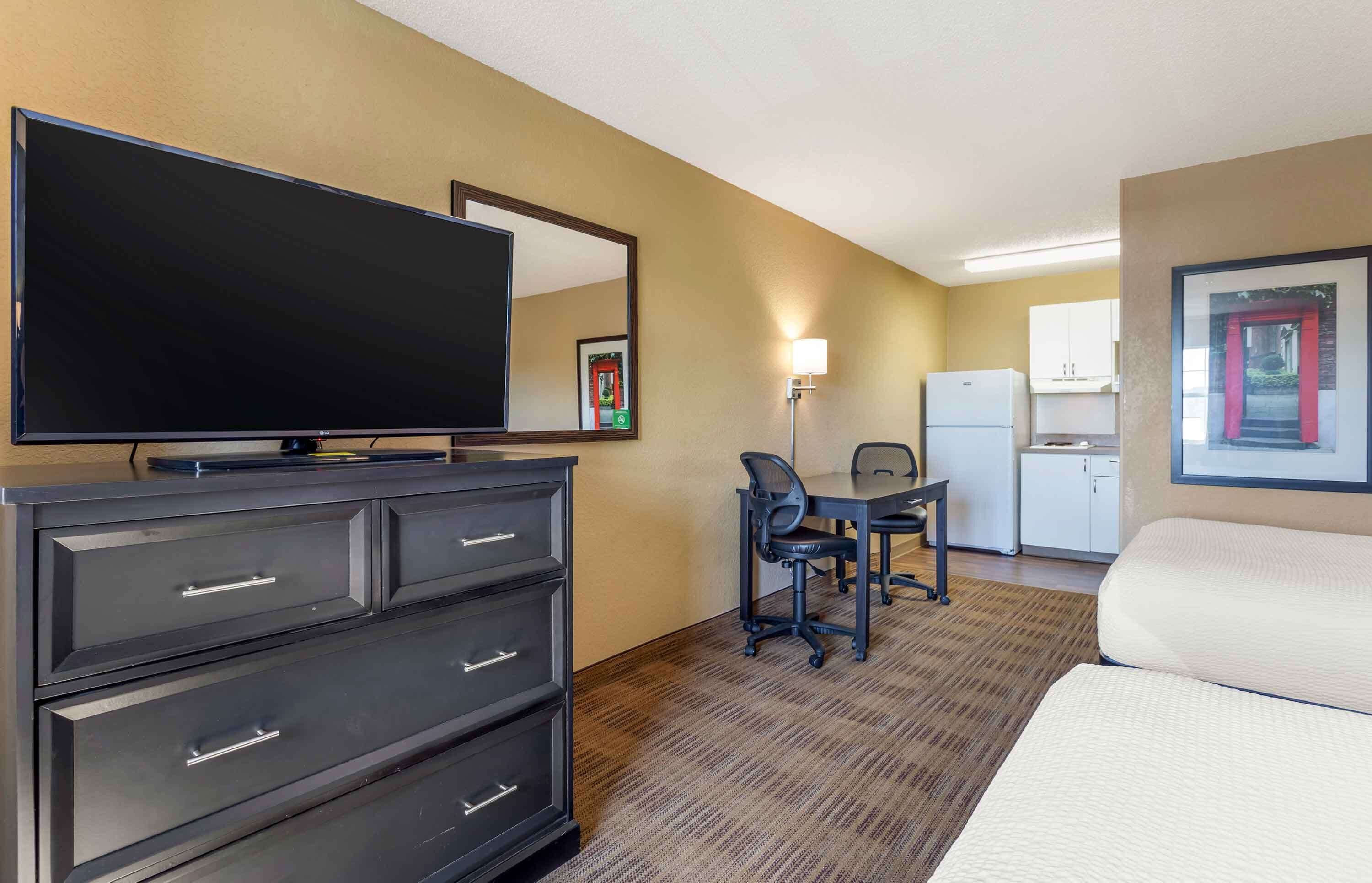 Une chambre d’hôtel équipée d’un grand téléviseur à écran plat, d’un bureau avec une chaise, d’un réfrigérateur, d’un four à micro-ondes, d’un lit et d’une commode.