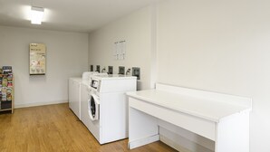 A laundry room with a washing machine, dryer, and a bulletin board with laundry-related information. - HomeTowne Studios By Red Roof Denver - Glendale/ Cherry Creek (Glendale)