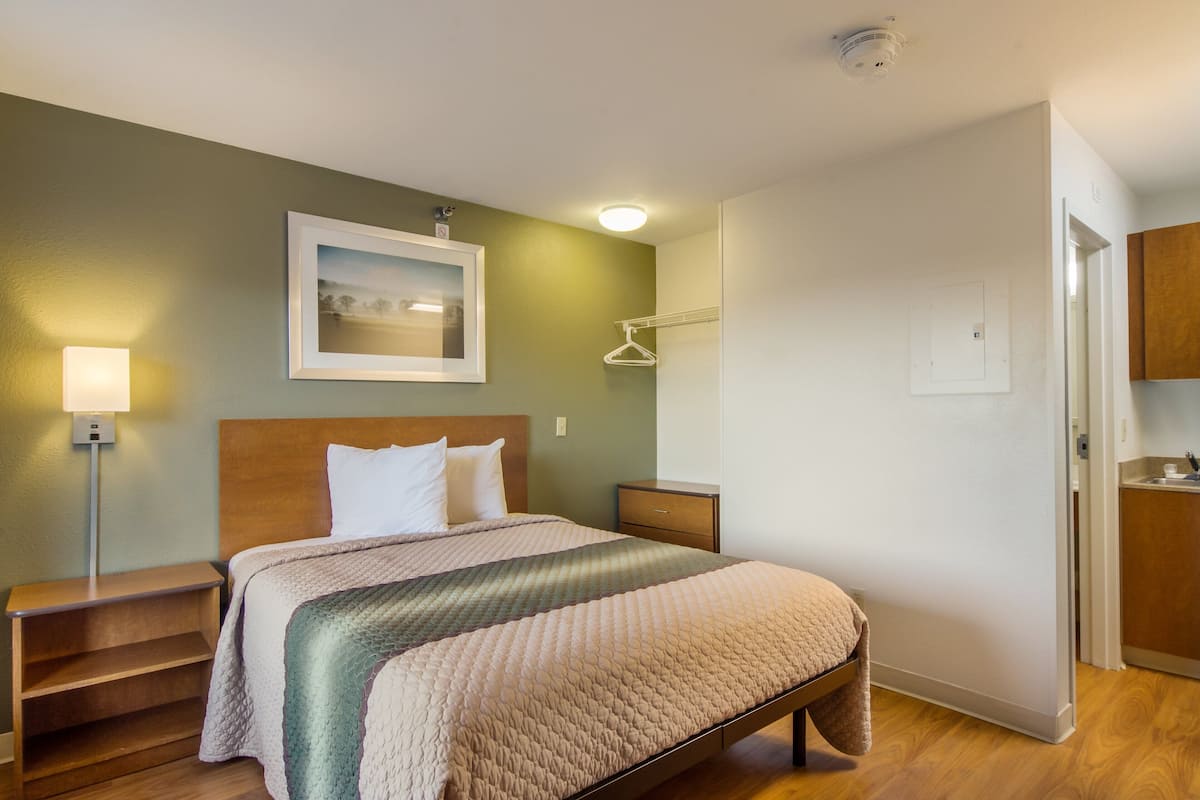 A hotel room with a bed, bedside table, lamp, and a framed picture on the wall.