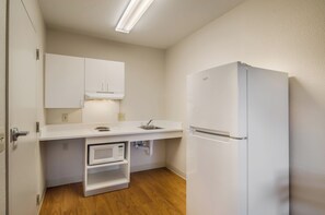 A compact kitchen with white cabinetry, a built-in microwave, a sink, and a refrigerator. - HomeTowne Studios By Red Roof Denver - Glendale/ Cherry Creek (Glendale)