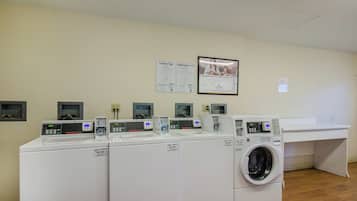 A laundry facility with multiple washing machines and dryers, a wall-mounted sign with laundry tips, and a framed advertisement.