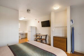 A compact hotel room with a bed, a desk, a chair, a television, and a wardrobe.