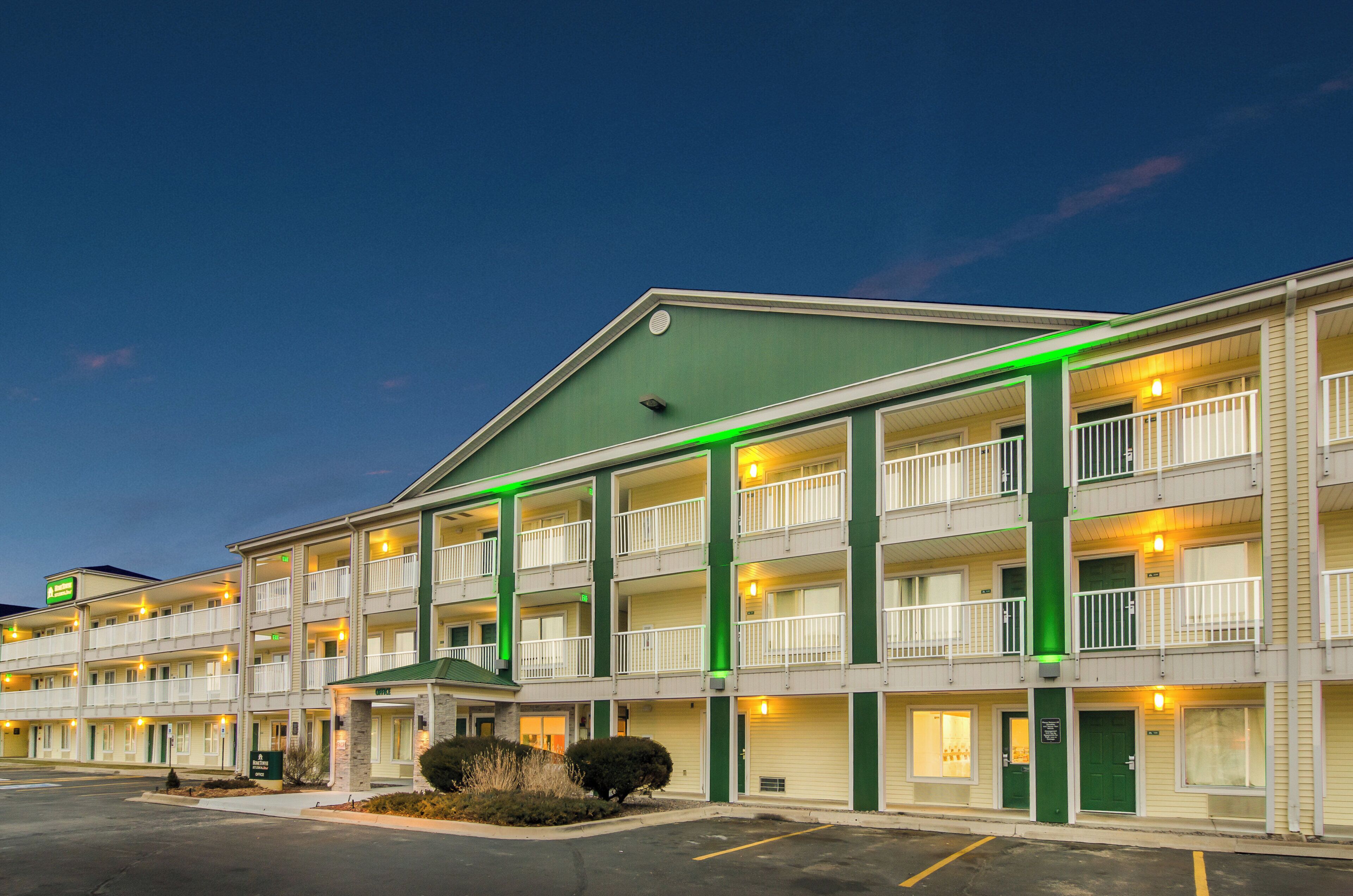 A multi-story motel with a green roof, multiple balconies, and a parking lot.
