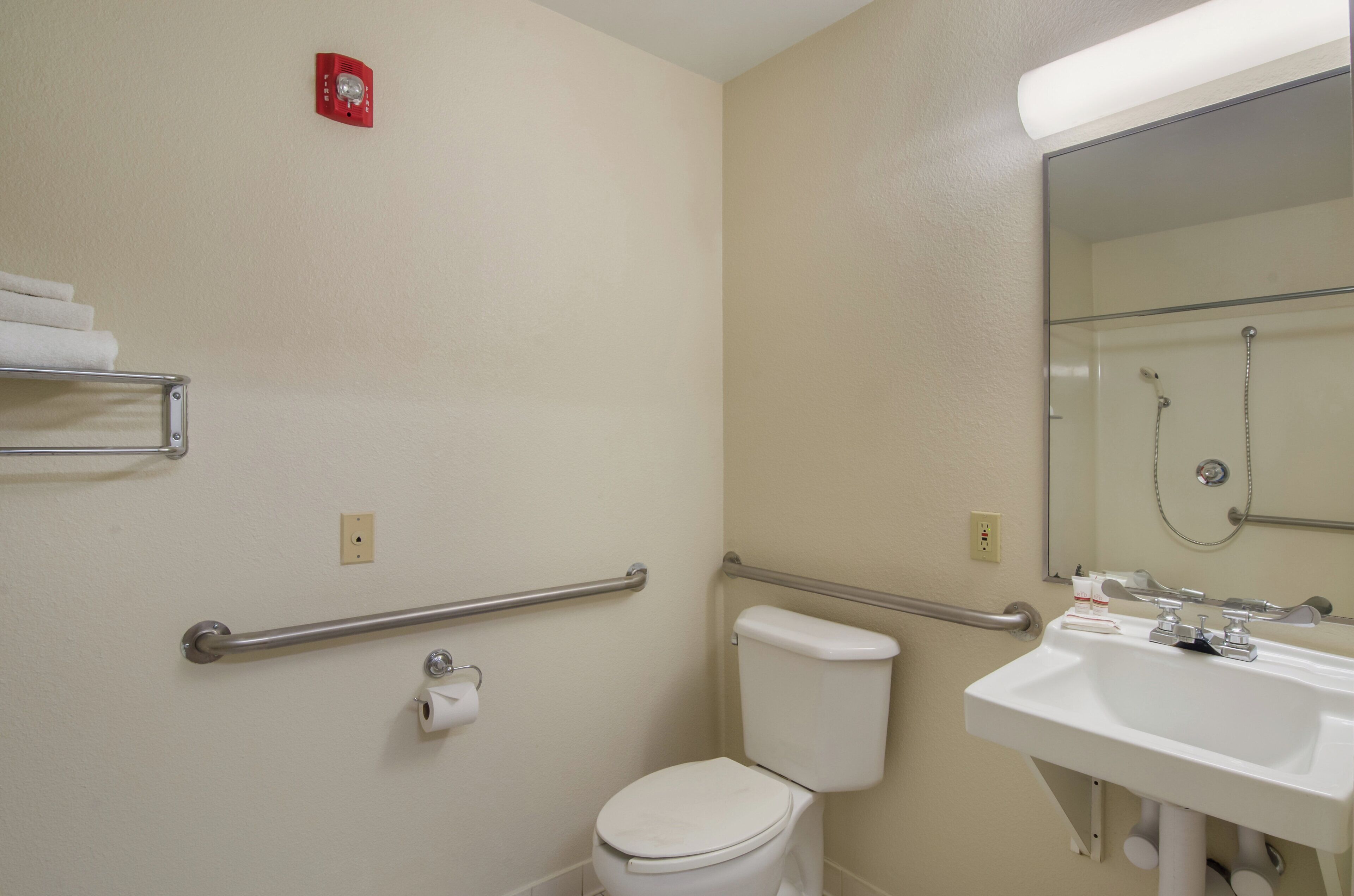 A bathroom with a toilet, a sink, a mirror, a towel rack, and a handrail.