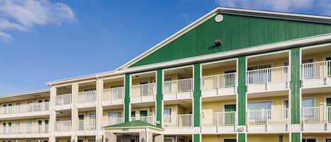 Um motel com vários andares, teto verde e paredes externas brancas, com varandas e entrada central.