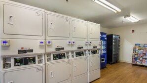 A laundry facility with multiple washing machines and dryers, payment card readers, and a vending machine. - HomeTowne Studios By Red Roof Denver - Glendale/ Cherry Creek (Glendale)