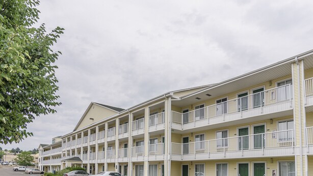A multi-story motel with balconies, a parking lot, and a grassy area. - HomeTowne Studios By Red Roof Denver - Glendale/ Cherry Creek (Glendale)
