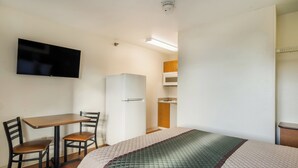 A compact hotel room with a bed, a desk with a chair, a television, a refrigerator, and a microwave. - HomeTowne Studios By Red Roof Denver - Glendale/ Cherry Creek (Glendale)