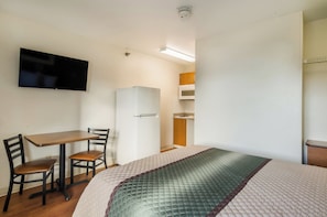 A compact hotel room with a bed, a desk with a chair, a television, a refrigerator, and a microwave. - HomeTowne Studios By Red Roof Denver - Glendale/ Cherry Creek (Glendale)
