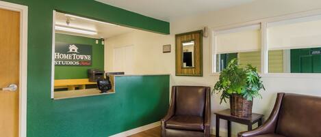 A reception area with a green wall, a reception desk, two leather chairs, a small table with a plant, and a mirror.