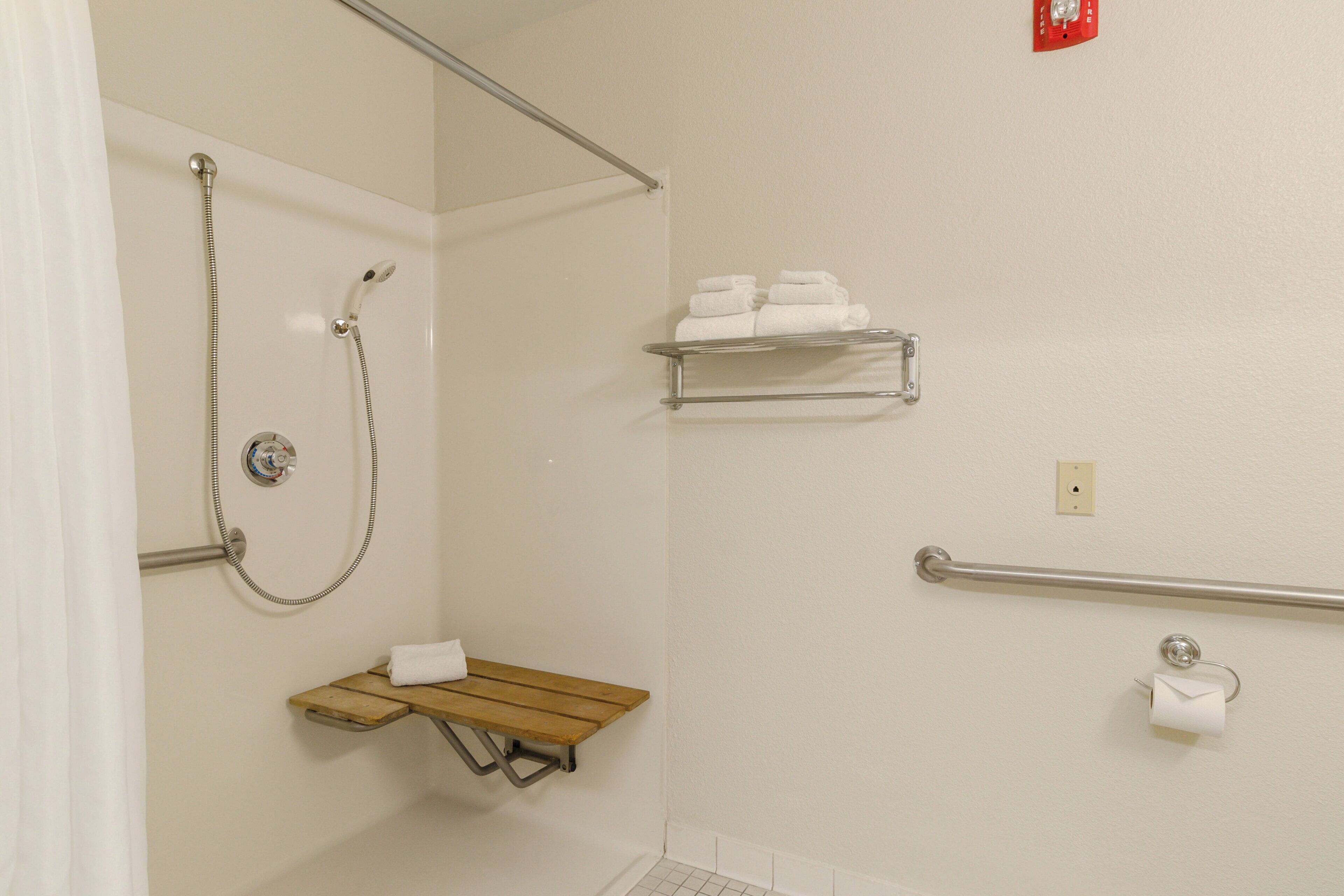A bathroom with a shower, a towel rack, a toilet paper holder, and a shelf with towels.
