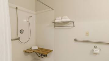 A bathroom with a shower, a towel rack, a toilet paper holder, and a shelf with towels.
