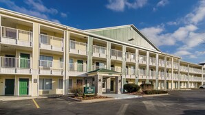 A multi-story motel with a central entrance, individual room doors, and a parking lot. - HomeTowne Studios By Red Roof Denver - Glendale/ Cherry Creek (Glendale)