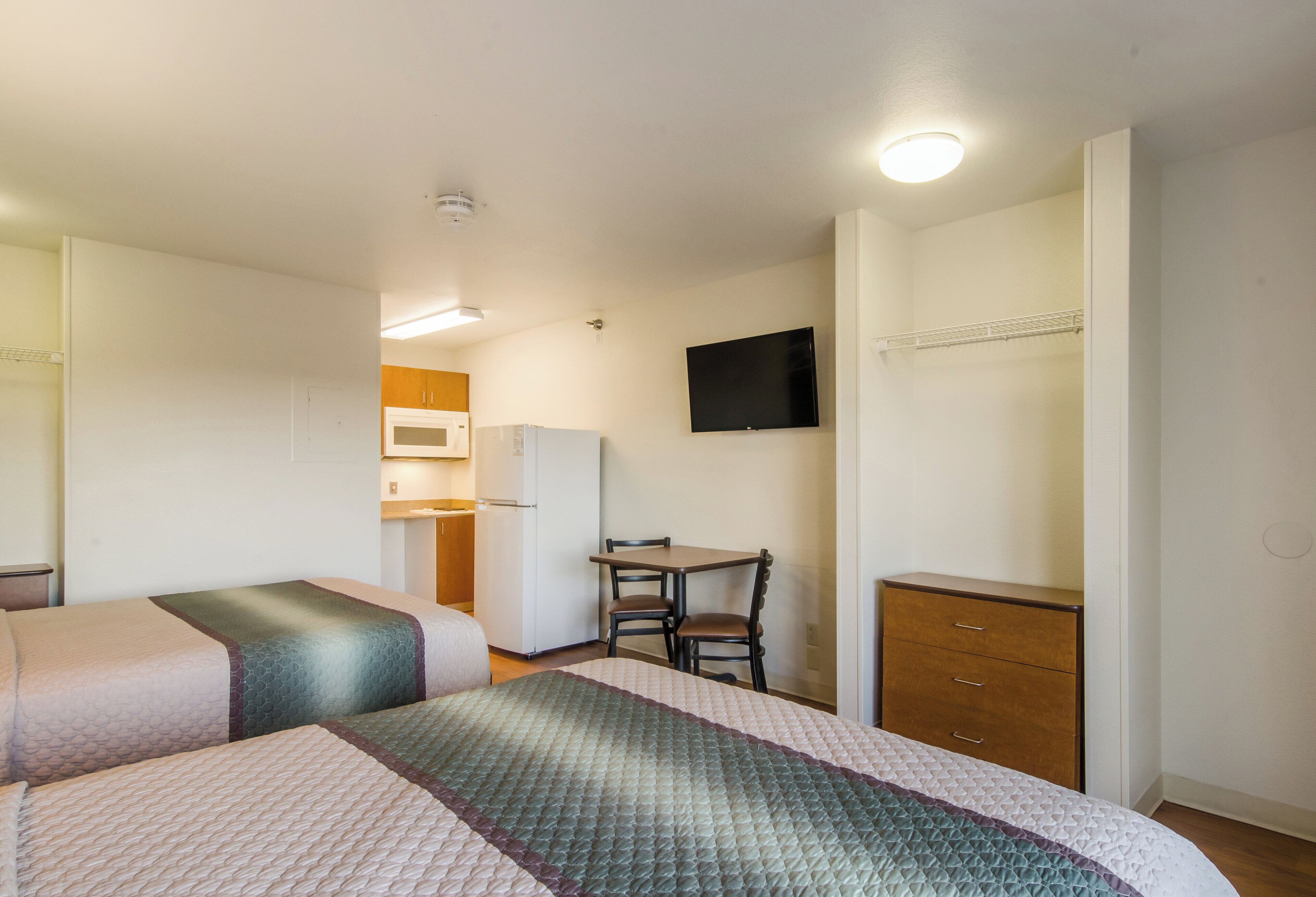 Een hotelkamer met twee bedden, een eettafeltje, een stoel, een televisie en een kledingkast.