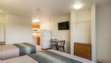Een hotelkamer met twee bedden, een eettafeltje, een stoel, een televisie en een kledingkast.