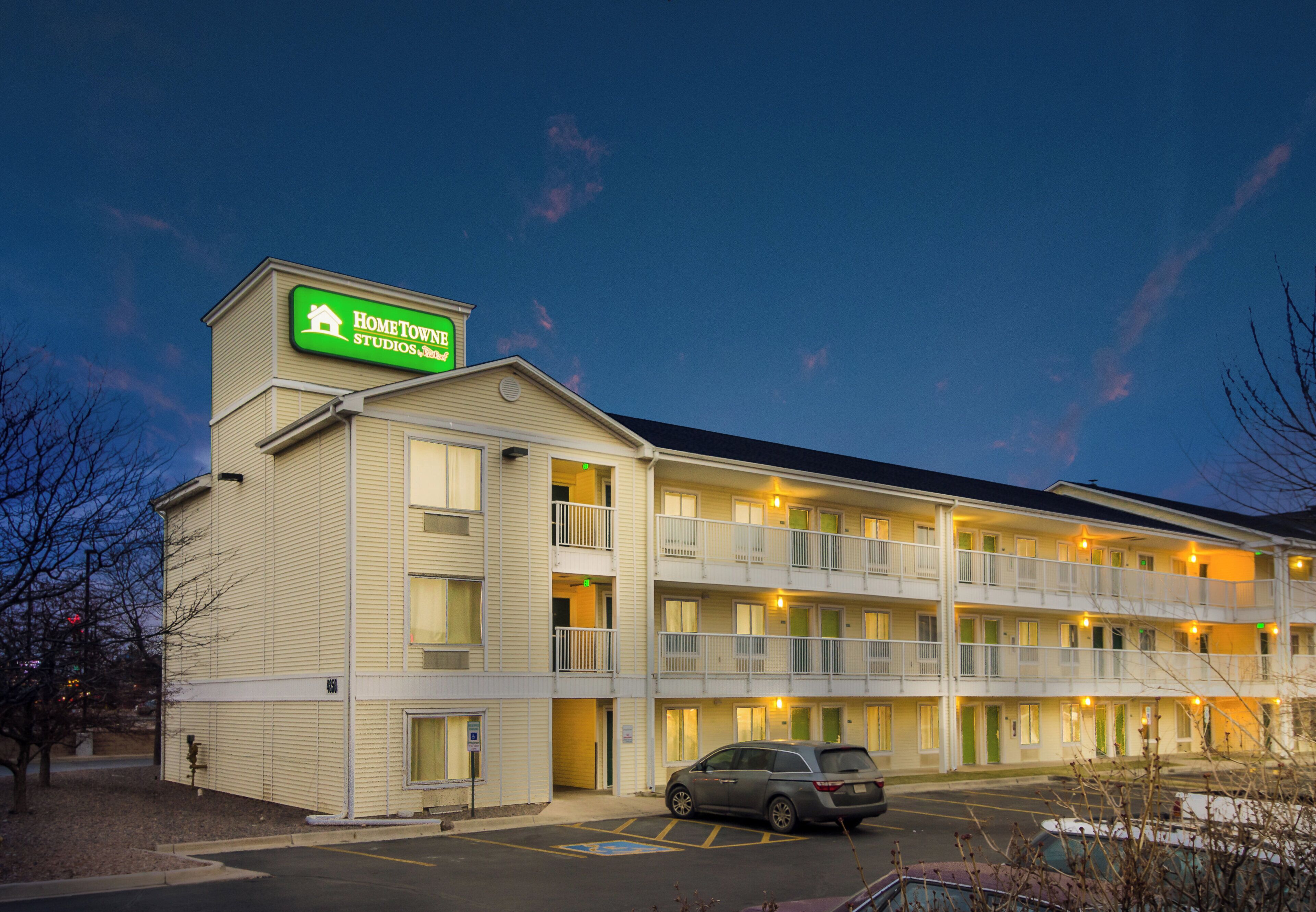 Een meerlaags motel met een groen bord, meerdere balkons en een parkeerplaats.