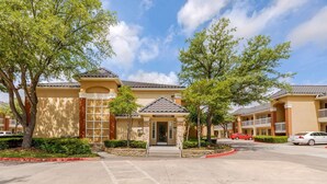 A hotel with a central entrance, multiple balconies, and a parking area. - Extended Stay America Suites Dallas Las Colinas Carnaby St (Irving)