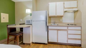 A compact kitchen with a refrigerator, microwave, and wooden cabinets. - Extended Stay America Suites Dallas Las Colinas Carnaby St (Irving)