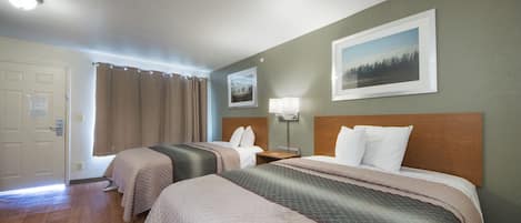 A hotel room with two beds, a wooden floor, a door, a window with curtains, and a wall-mounted picture.