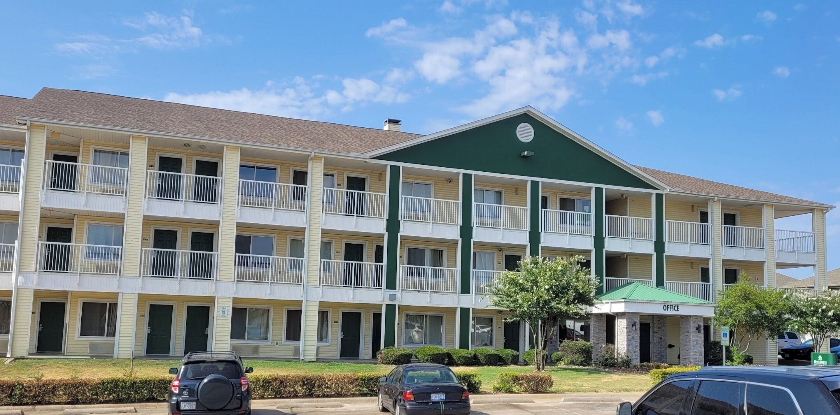 A multi-story motel with balconies, a green roof, and a parking lot.