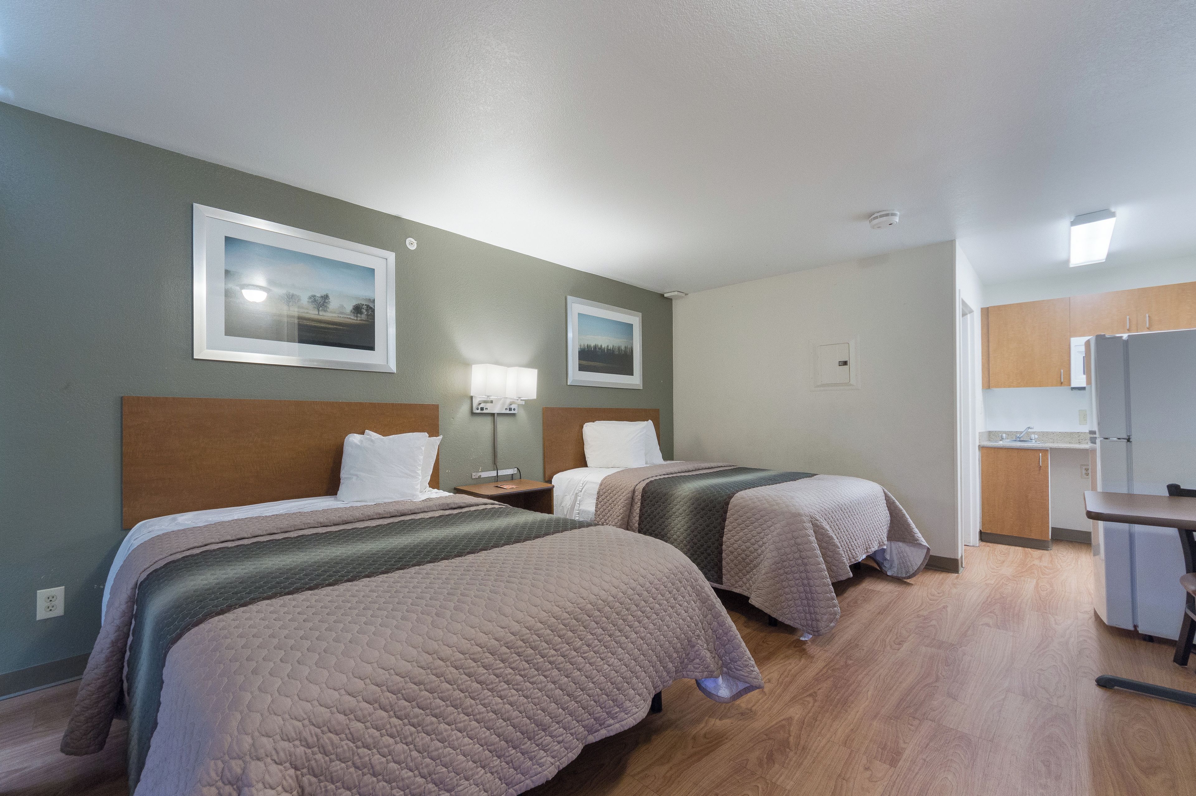 A hotel room with two beds, a desk, a chair, a lamp, and a picture on the wall.