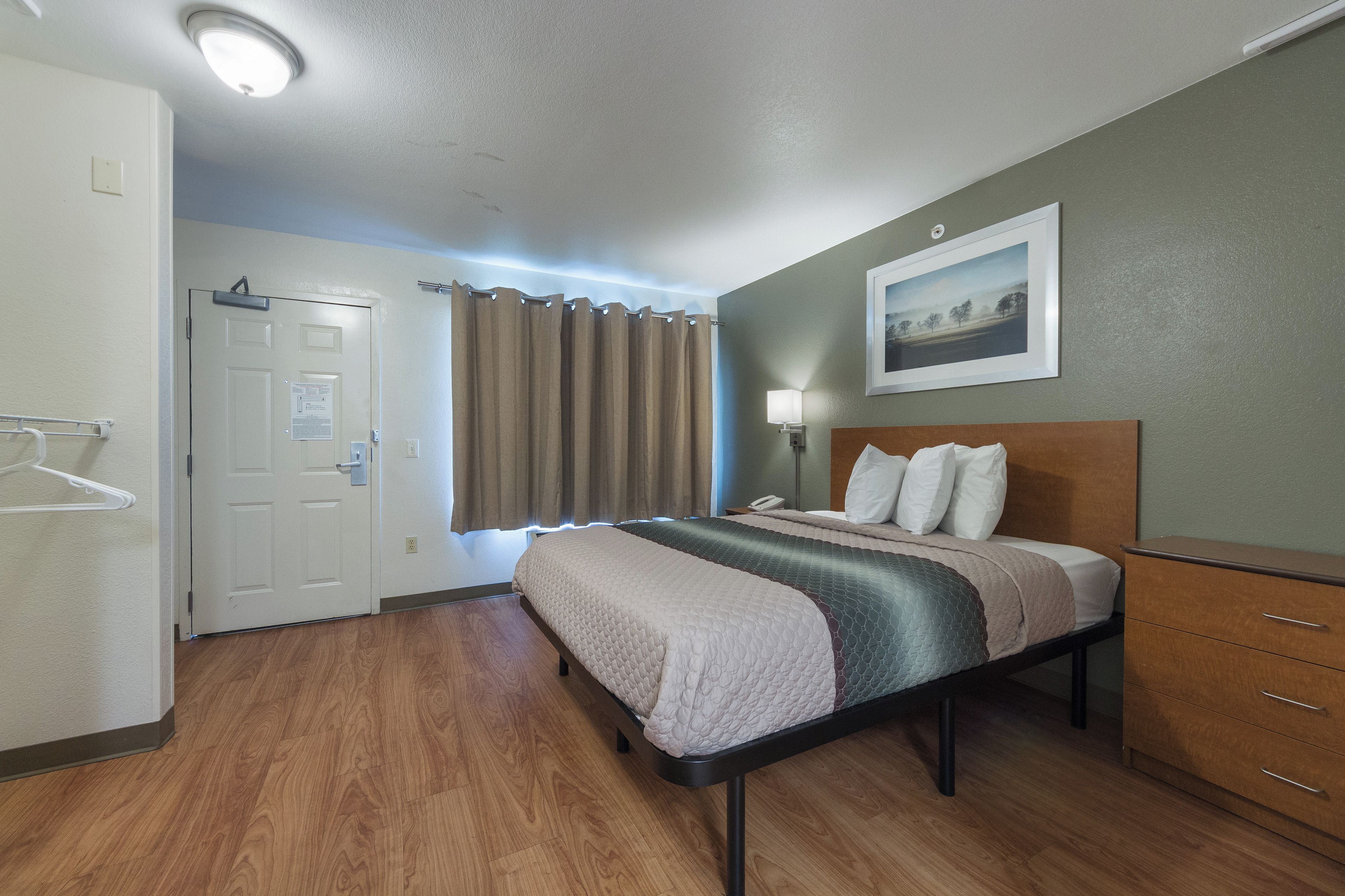 Une chambre d’hôtel avec un lit, une table de chevet, une lampe, un tableau au mur et une porte.