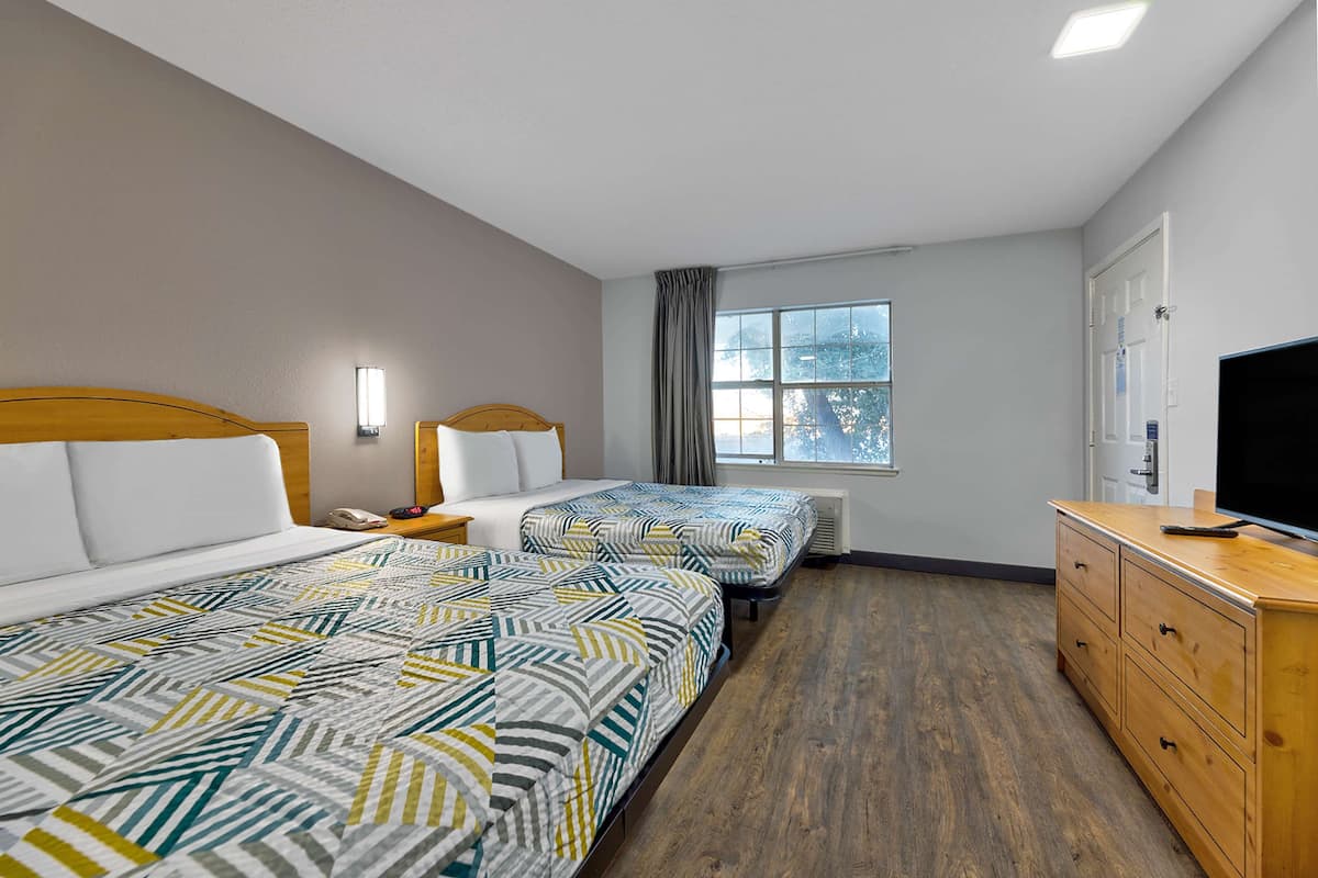 Een hotelkamer met twee bedden, een houten dressoir, een televisie en een raam met uitzicht op bomen.