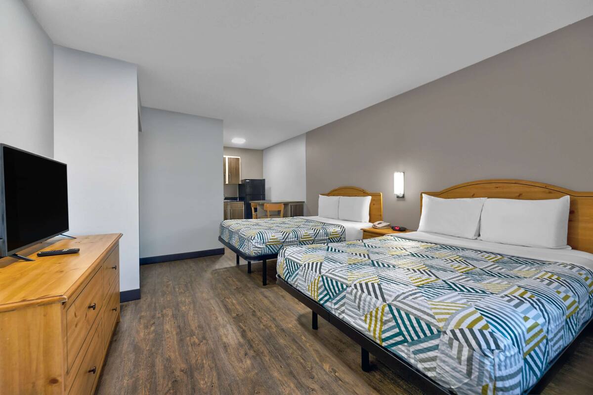 Een hotelkamer met twee bedden, een houten dressoir, een televisie en een kitchenette op de achtergrond.