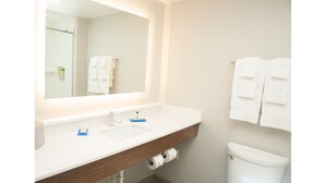 A bathroom with a white sink, a mirror, and a toilet. There are towels hanging on the wall.