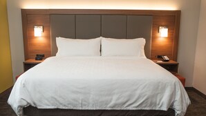 A large bed with a wooden headboard, two bedside tables with lamps, and a digital clock on one of the tables.