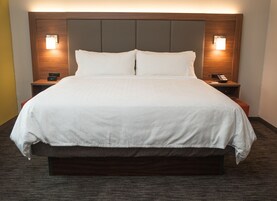 Una cama grande con cabecera de madera, dos mesitas de noche con lámparas y un reloj digital en una de ellas.