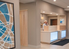 Un área de recepción con una puerta de madera, un mostrador de recepción y una obra de arte abstracta enmarcada en la pared.