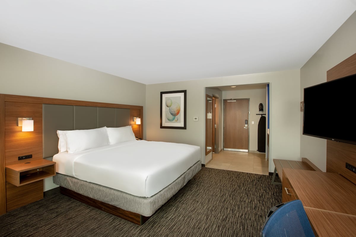 A hotel room with a large bed, bedside tables, a flat-screen TV, and a desk with a chair.
