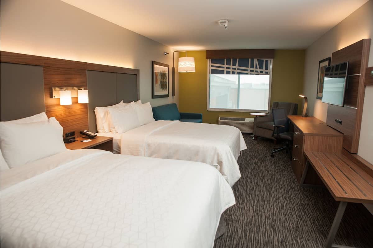 A hotel room with two beds, a desk, a chair, a TV, and a window with a view.