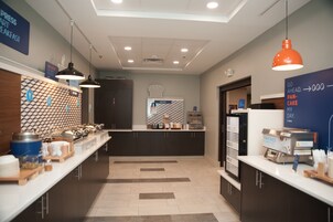 Un área de desayuno moderna con una panadería, una máquina de café y un cartel que indica una sala de prensa.