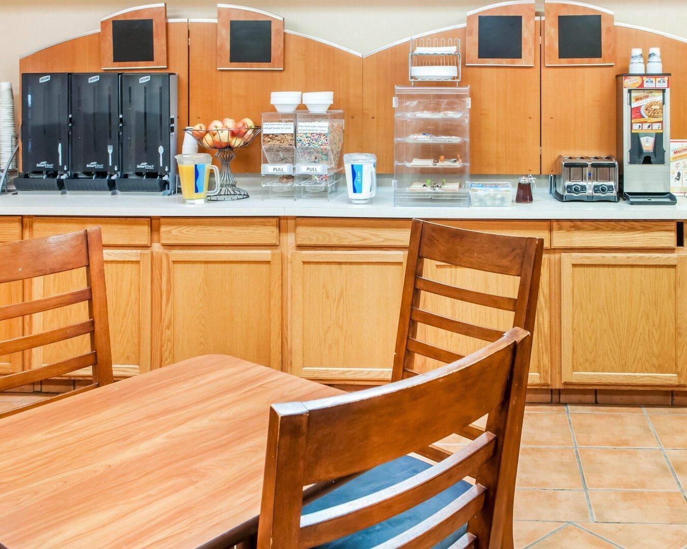 Una cocina con armarios de madera, una mesa de comedor, sillas, una cafetera, un tostador y un refrigerador.