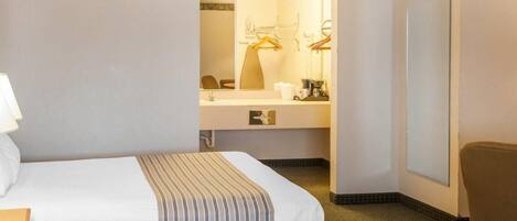 A hotel room with two beds, a desk, a chair, a mirror, and a bathroom visible through a glass door.