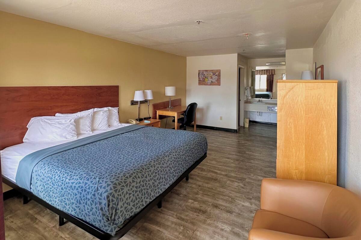 Habitación de hotel con una cama, un escritorio, una silla y un baño visible al fondo.